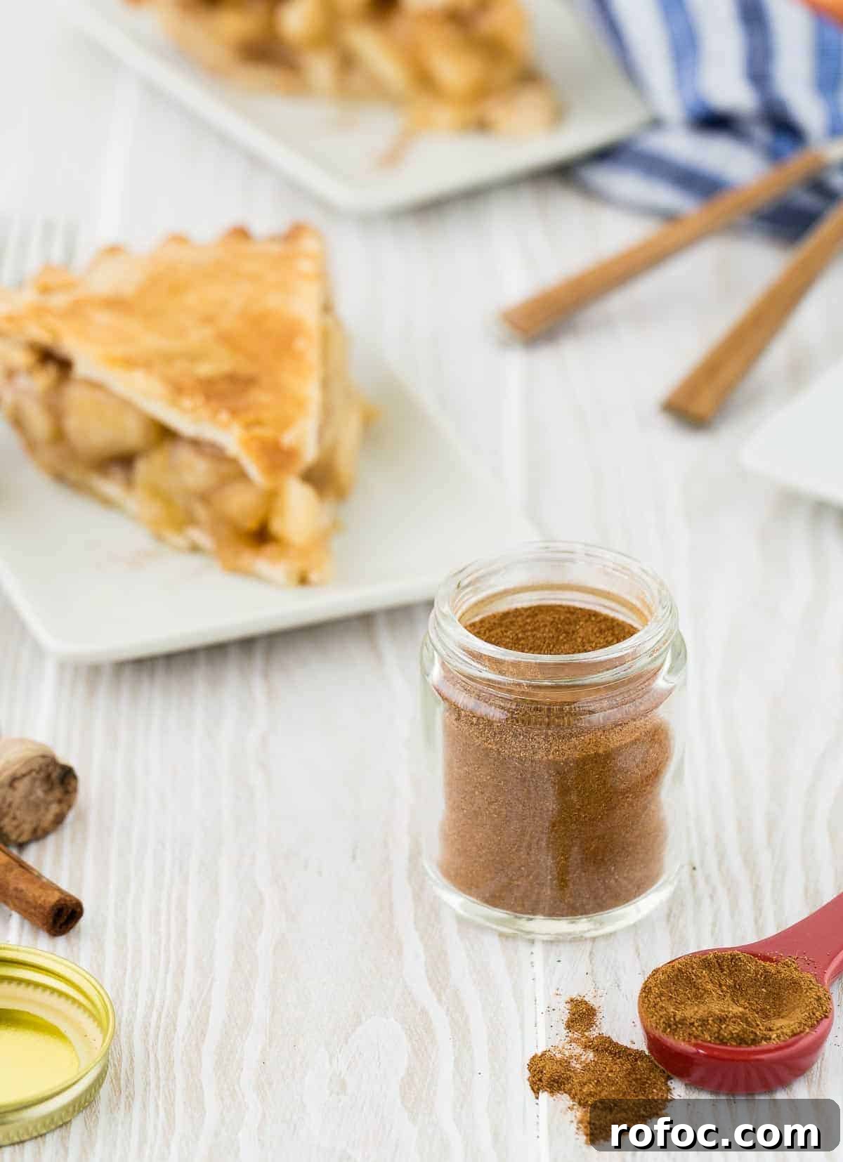Homemade Apple Pie Spice Mix You Can Make in Minutes 3 Wooden background with apple pie spice in a small jar. Also pictured are cinnamon sticks and apple pie on a white plate.