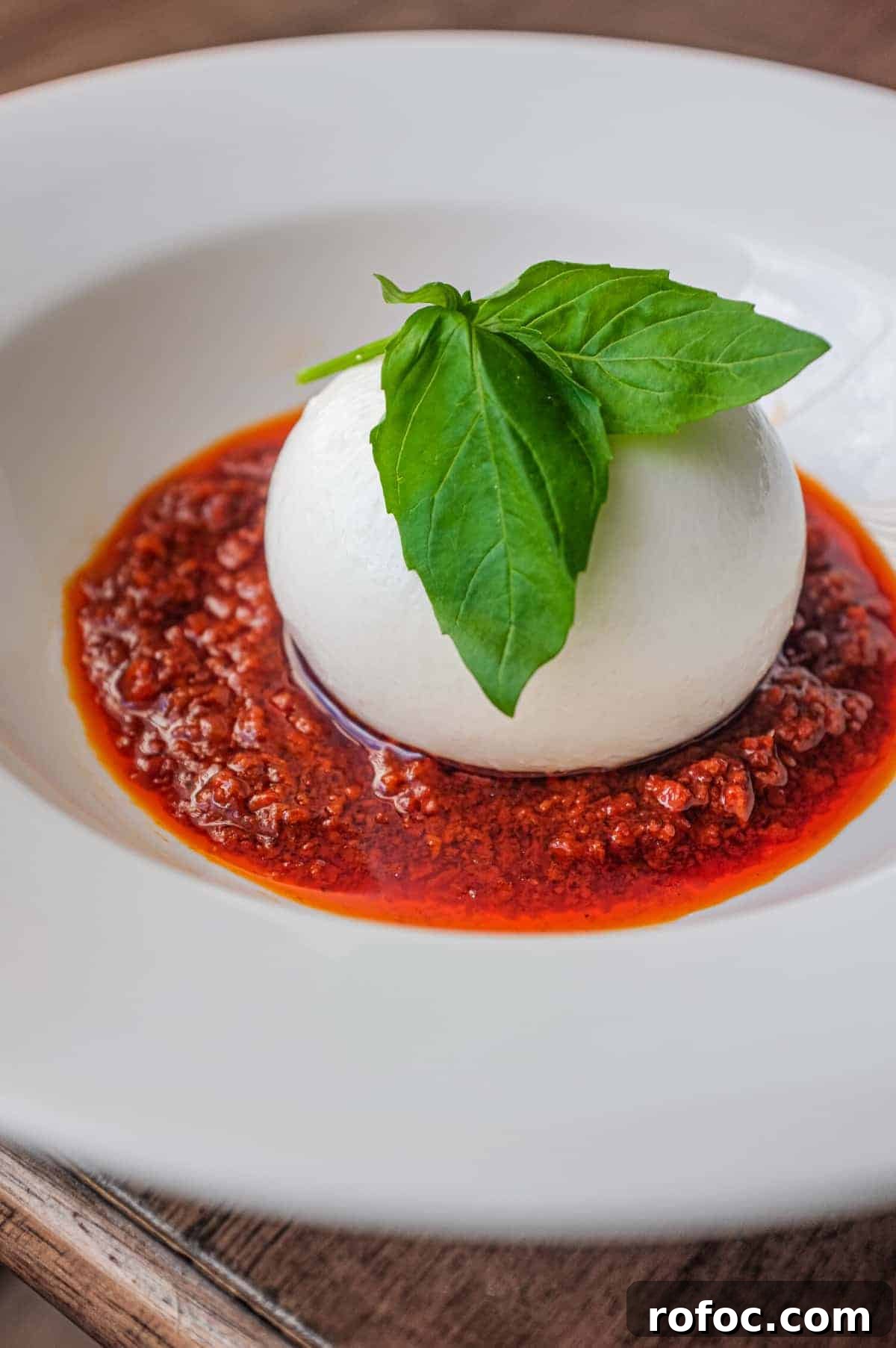 Nduja with Burrata | cookeatworld.com A plate of nduja sausage in liquid form, topped with a ball of burrata cheese and garnished with a small sprig of basil. A fork sits in the sauce.