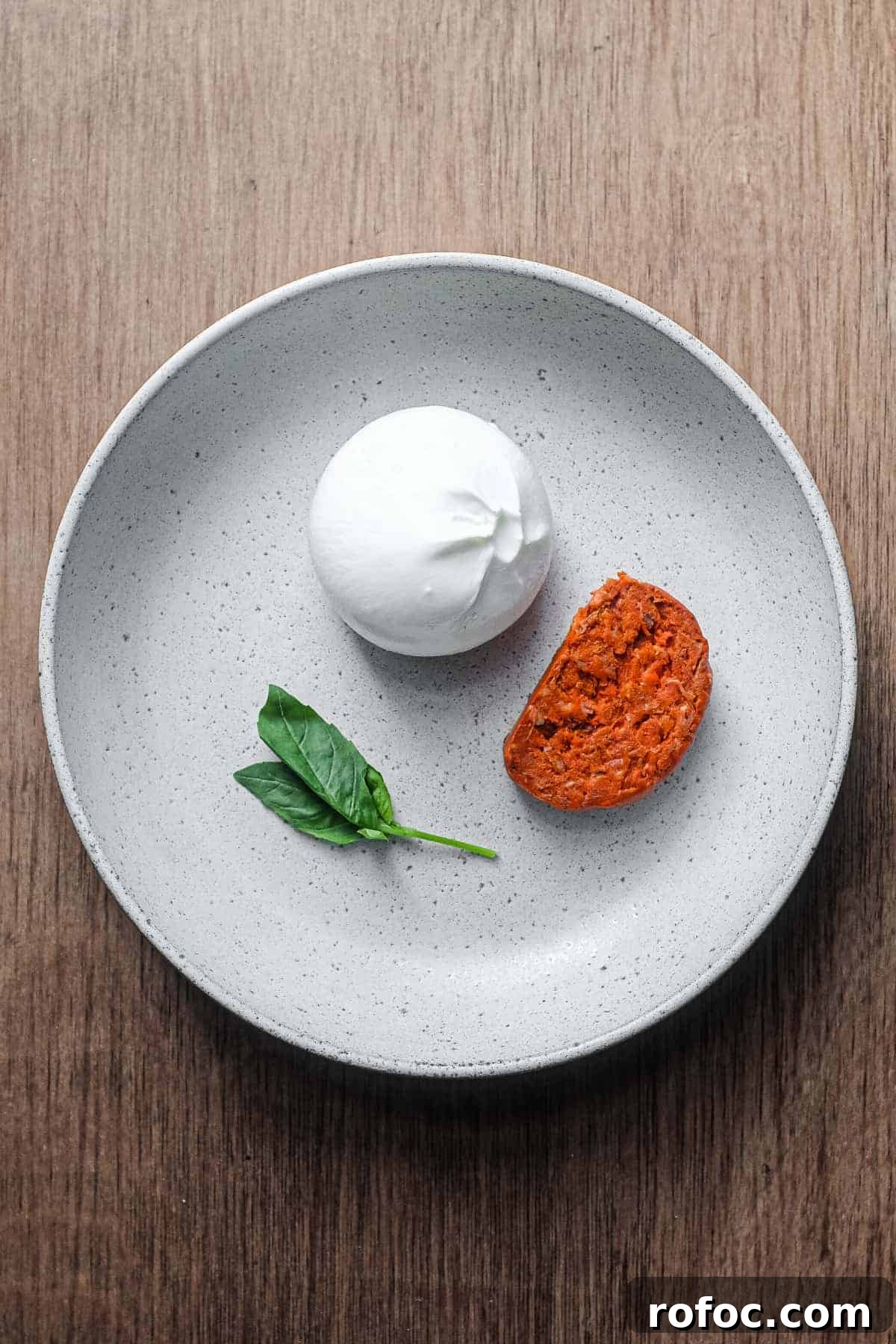 Nduja with Burrata | cookeatworld.com A plate holding a slice of nduja sausage, a burrata and a small sprig of basil.