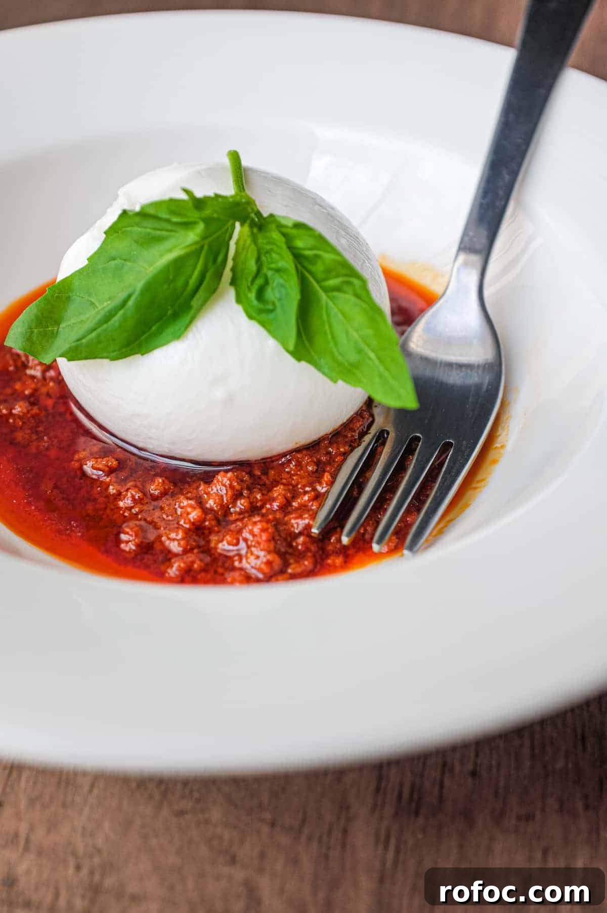 Nduja with Burrata | cookeatworld.com A plate of nduja sausage in liquid form, topped with a ball of burrata cheese and garnished with a small sprig of basil. A fork sits in the sauce.