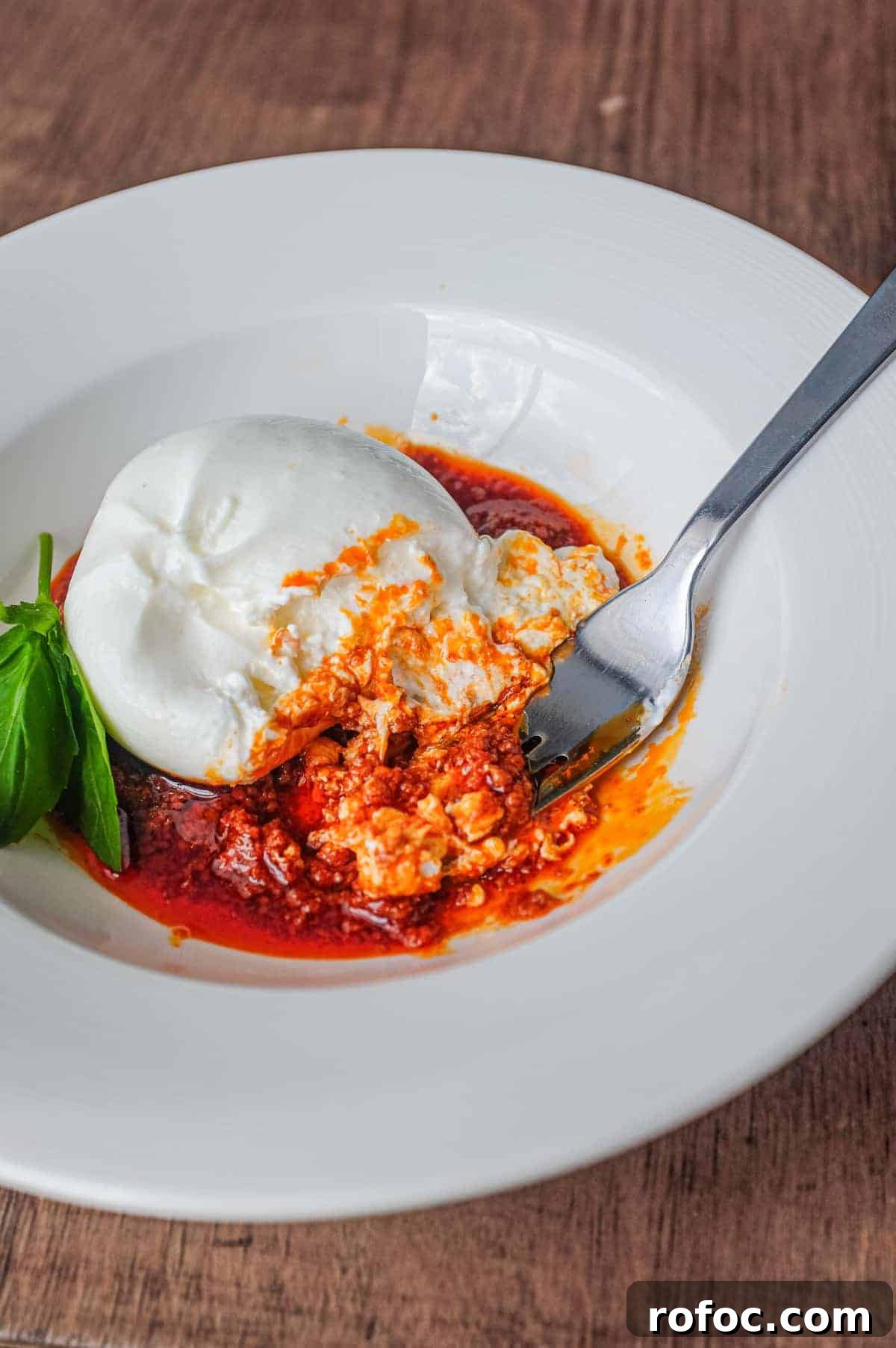 Nduja with Burrata | cookeatworld.com A plate of nduja sausage in liquid form, topped with a ball of burrata cheese and garnished with a small sprig of basil. A fork sits in the sauce.