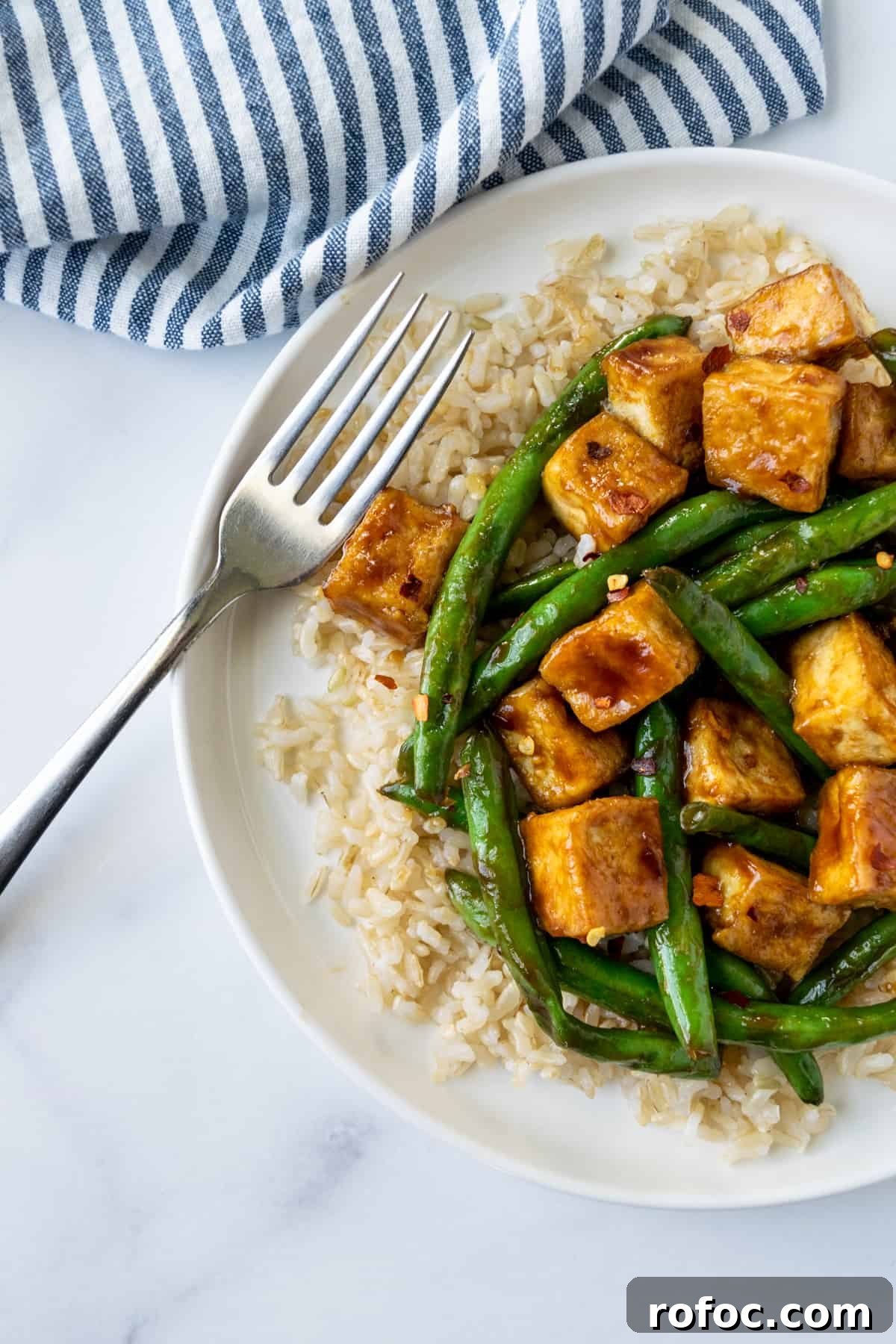 Teriyaki Tofu Stir-Fry with Crispy Green Beans 3 Teriyaki Tofu Stir Fry with Green Beans on a white plate on a table with a blue and white striped linen.