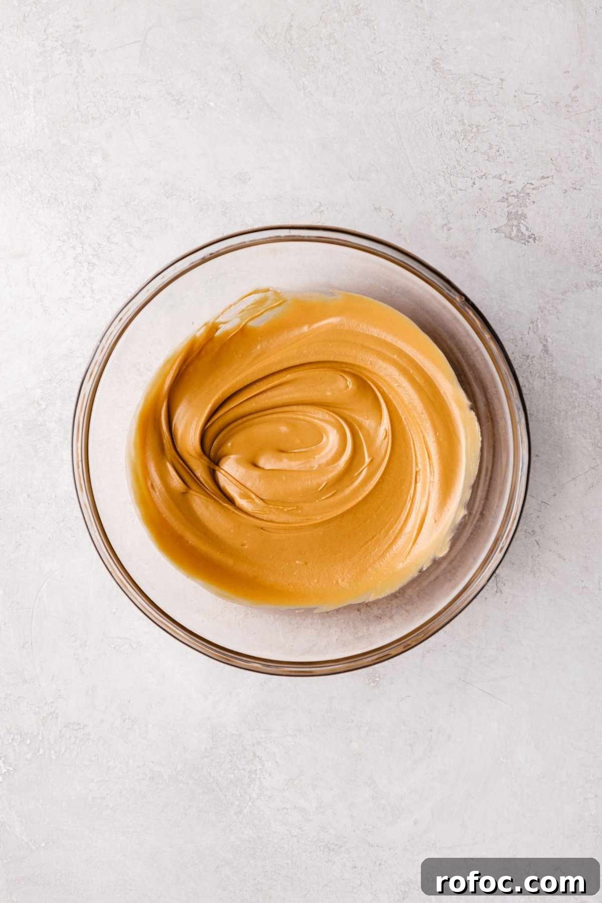 Melted butterscotch chips in a small glass bowl on a white and grey textured background.