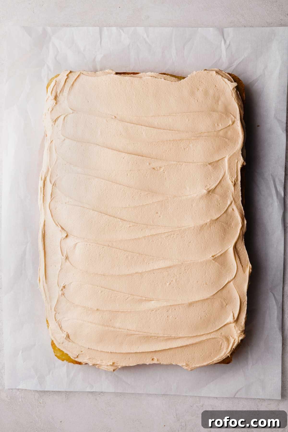 Frosted butterscotch krimpet sheet cake on a parchment paper lined white and grey textured background.