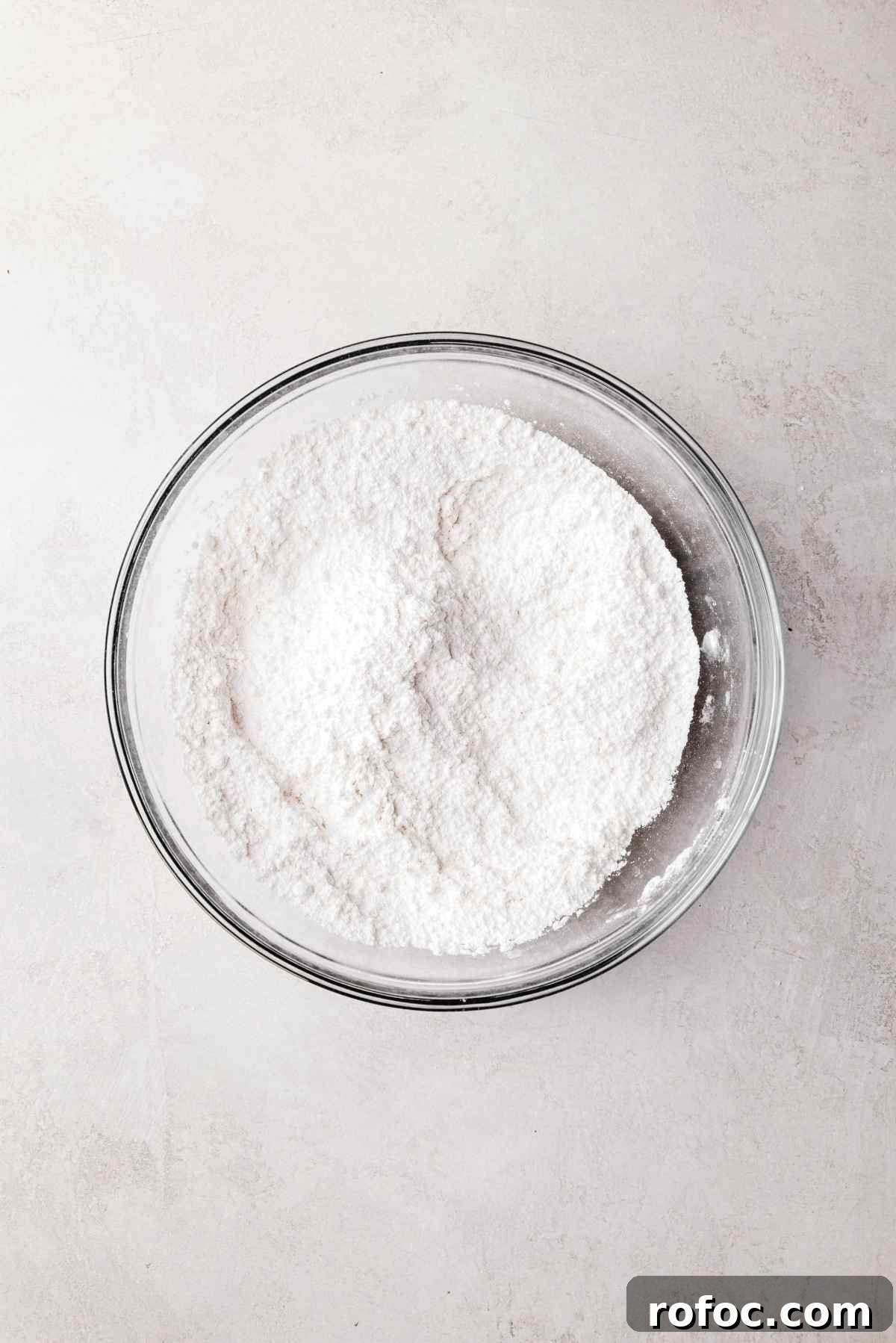Whisked cake flour, baking powder, and salt in a small glass mixing bowl on a white and grey textured background.