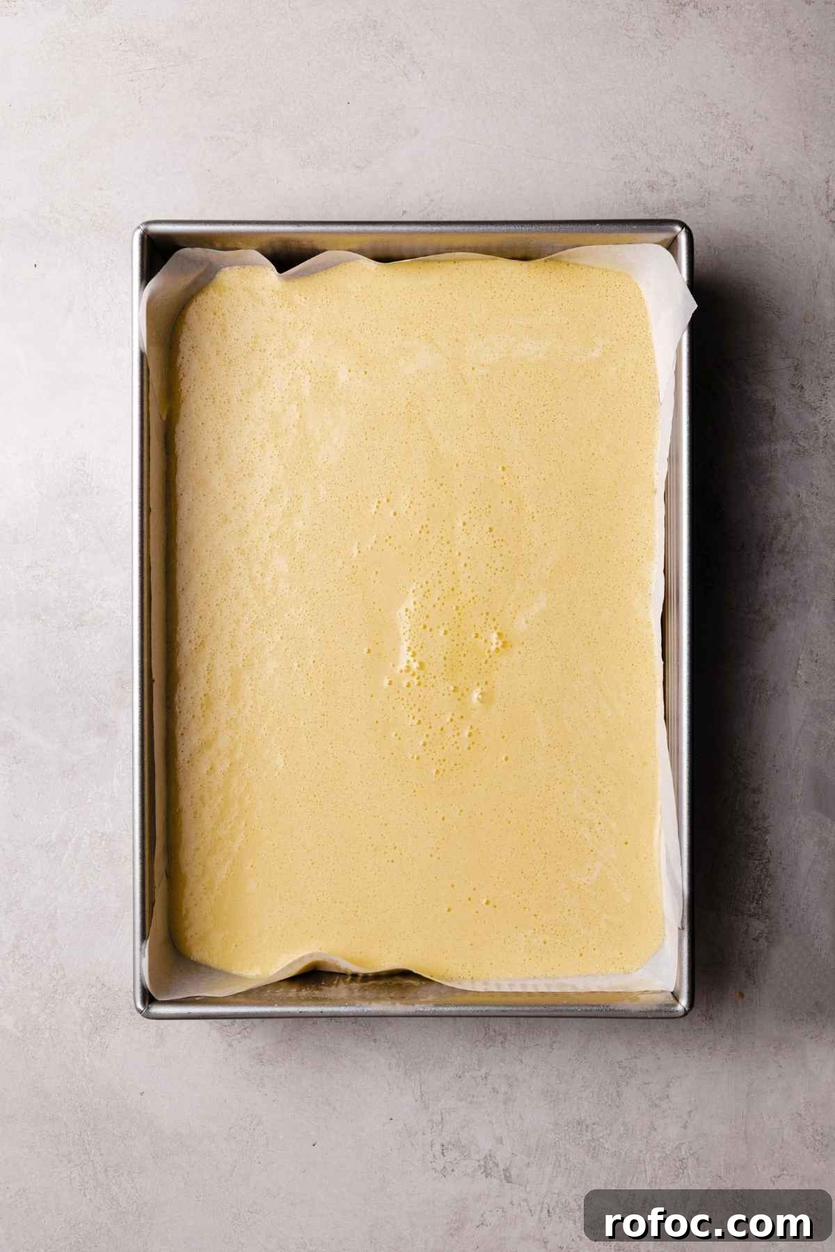Vanilla sponge cake batter transferred to a 13 by 9 inch metal baking pan lined with parchment paper.
