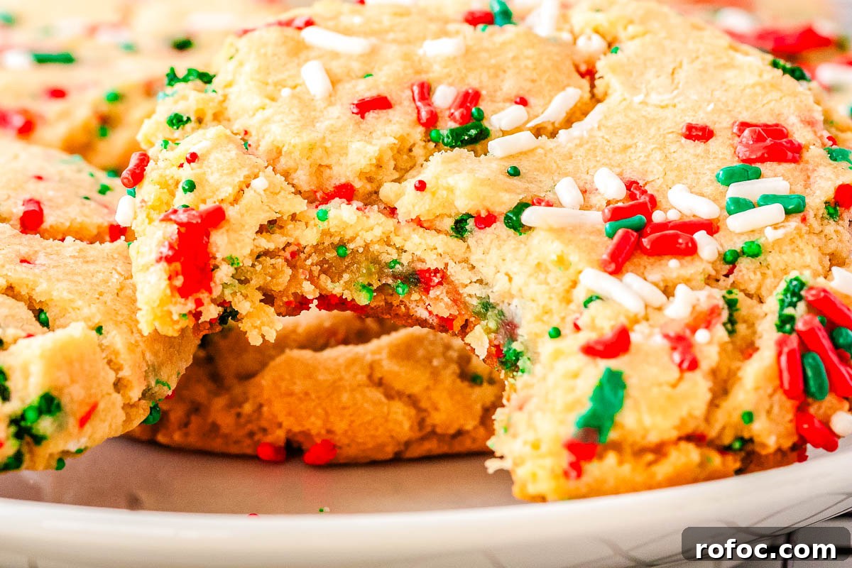 Close-up of a soft Christmas sprinkle sugar cookie with a bite taken out, showing chewy center and colorful sprinkles baked into the dough.