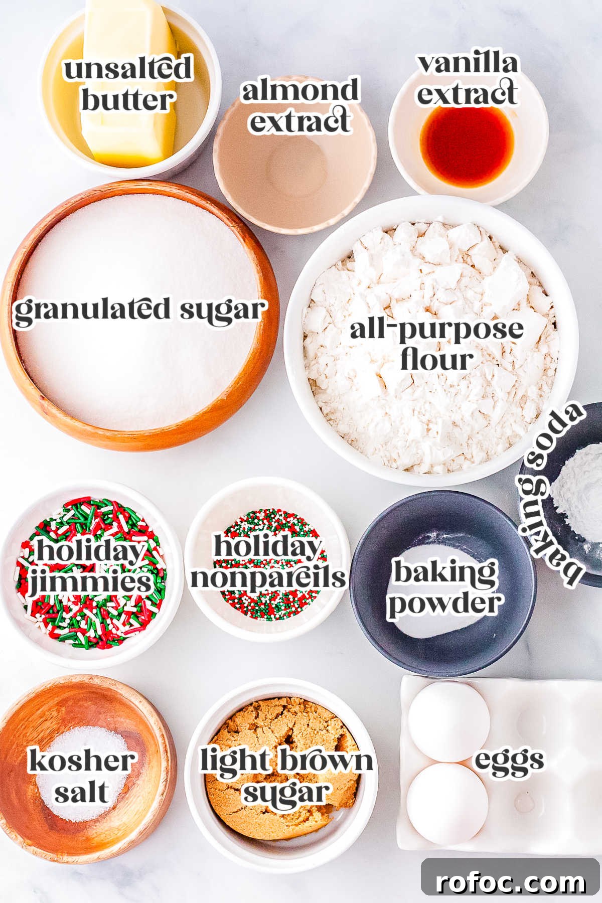 Measured ingredients for Christmas sprinkle sugar cookies including flour, sugars, butter, eggs, vanilla, almond extract, and colorful holiday sprinkles arranged in bowls.