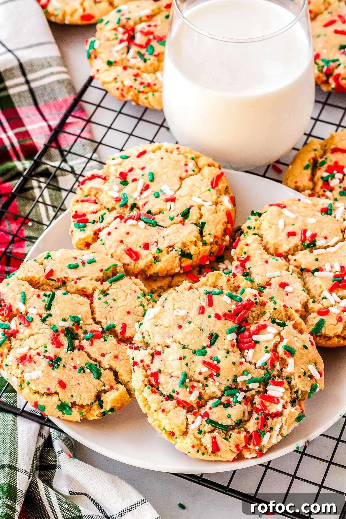 Plate of Christmas sprinkle sugar cookies next to a glass of milk on a cooling rack with festive red and green sprinkles, ready for holiday sharing.