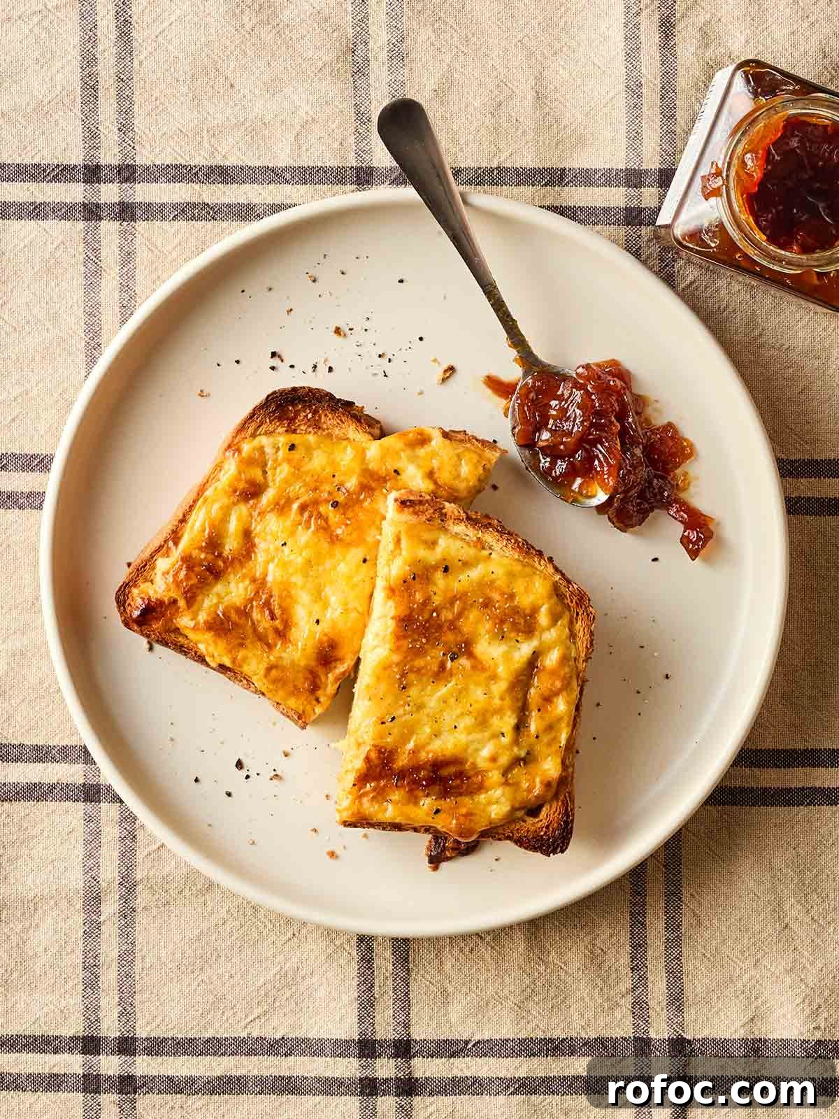 Classic Welsh Rarebit Recipe: Savory Cheese Toast with Ale 3 A plate with a slice of Welsh rarebit with a spoonful of chutney to the side, on a checked tablecloth.