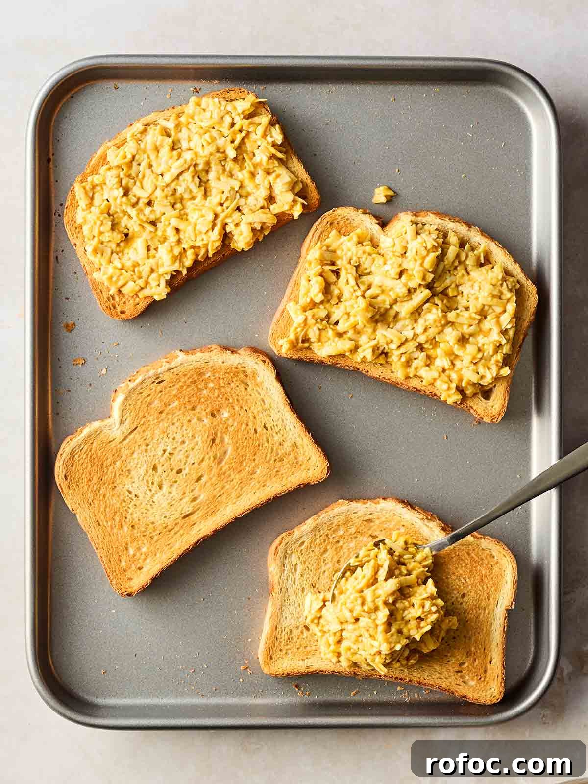Classic Welsh Rarebit Recipe: Savory Cheese Toast with Ale 6 An oven tray with four slices of toasted bread on and a cheese mixture on top. Welsh Rarebit going into the oven.
