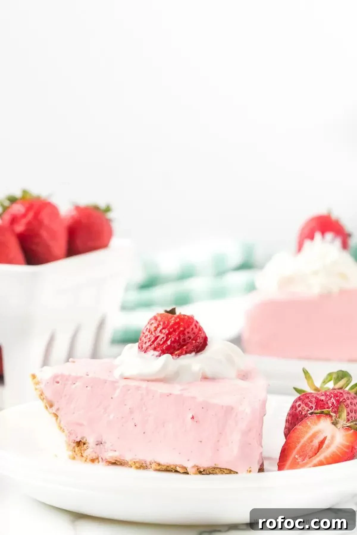 Strawberry jello pie recipe is an easy and classic dessert you can make in minutes. Retro Strawberry jello pie recipe is so light and fluffy and you only need 5 ingredients! Strawberry jello pie cool whip recipe with no bake graham cracker crust makes Strawberry jello pie easy. #dessertonadime #strawberryjellopierecipe Strawberry Jello pie with a side of slice strawberries on a white plate with a fork.