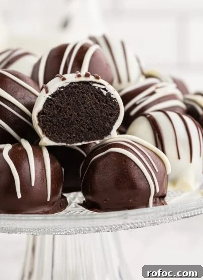 Oreo cookie balls piled on top of each other on a glass cake stand, single Oreo ball cut in half.