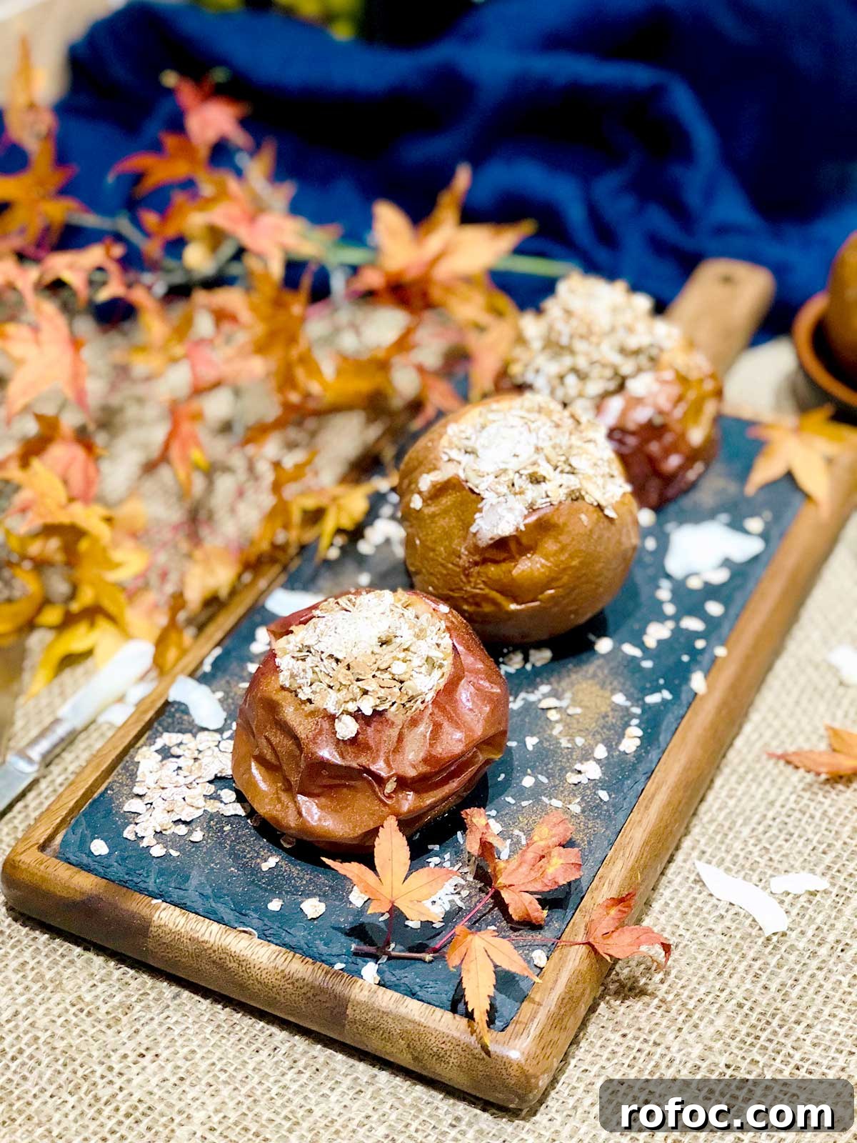 Baked Apples Stuffed with Cinnamon Oatmeal 2 Three baked apples with oatmeal on a blackboard with a wooden frame dusted with cinnamon and autumnal leaves for decoration.