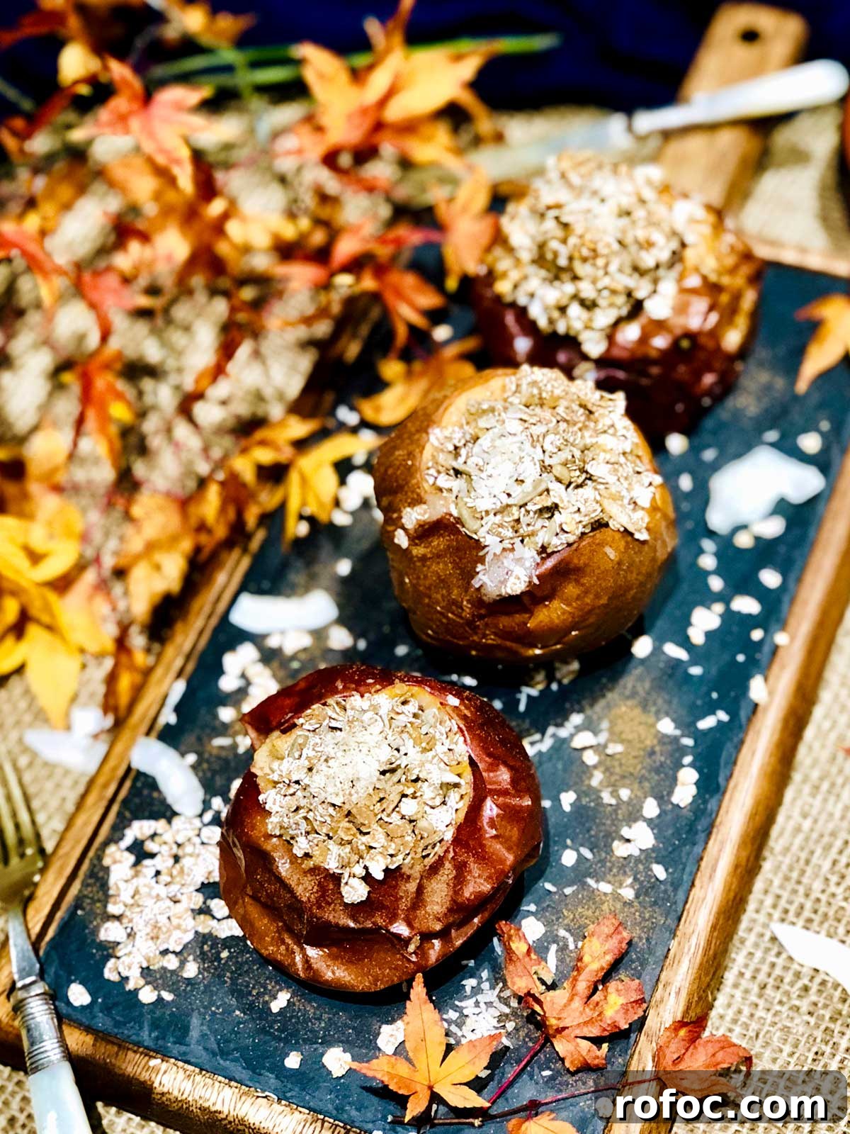 Baked Apples Stuffed with Cinnamon Oatmeal 3 Close up or birdseye of three baked apples stuffed with oatmeal and coconut flakes sprinkled over on a black and wooden frame board.