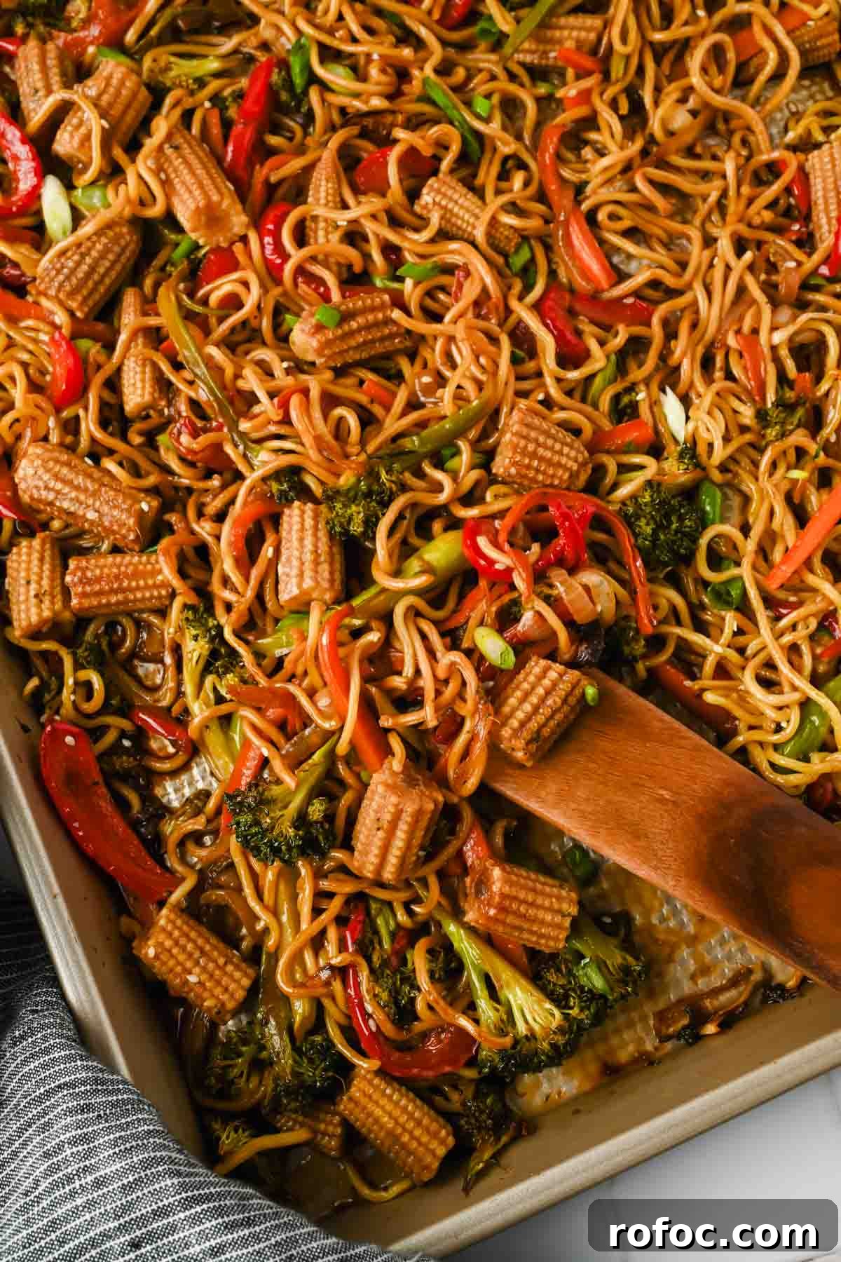Crispy Sheet-Pan Chow Mein: Quick One-Pan Asian Noodle Bake 2 sheet pan chow mein with broccoli, peppers and corn mixed on gold baking sheet.