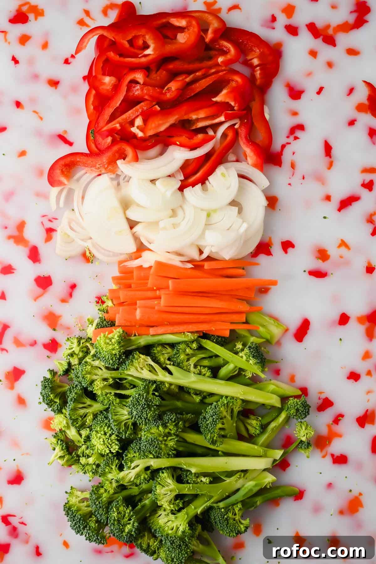 Crispy Sheet-Pan Chow Mein: Quick One-Pan Asian Noodle Bake 4 chopped broccoli, carrots, white onion and red bell pepper on speckled cutting board.