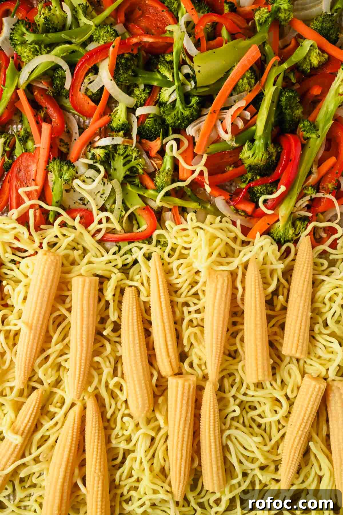 Crispy Sheet-Pan Chow Mein: Quick One-Pan Asian Noodle Bake 7 chopped raw broccoli, carrots, white onion, red bell pepper, noodles and corn on sheet pan.