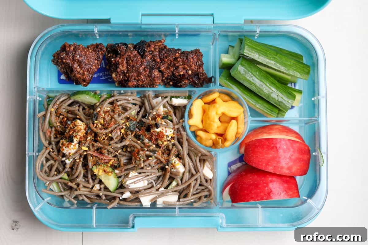 Photo of a bento style lunch box with the main compartment filled with this soba noodle recipe.