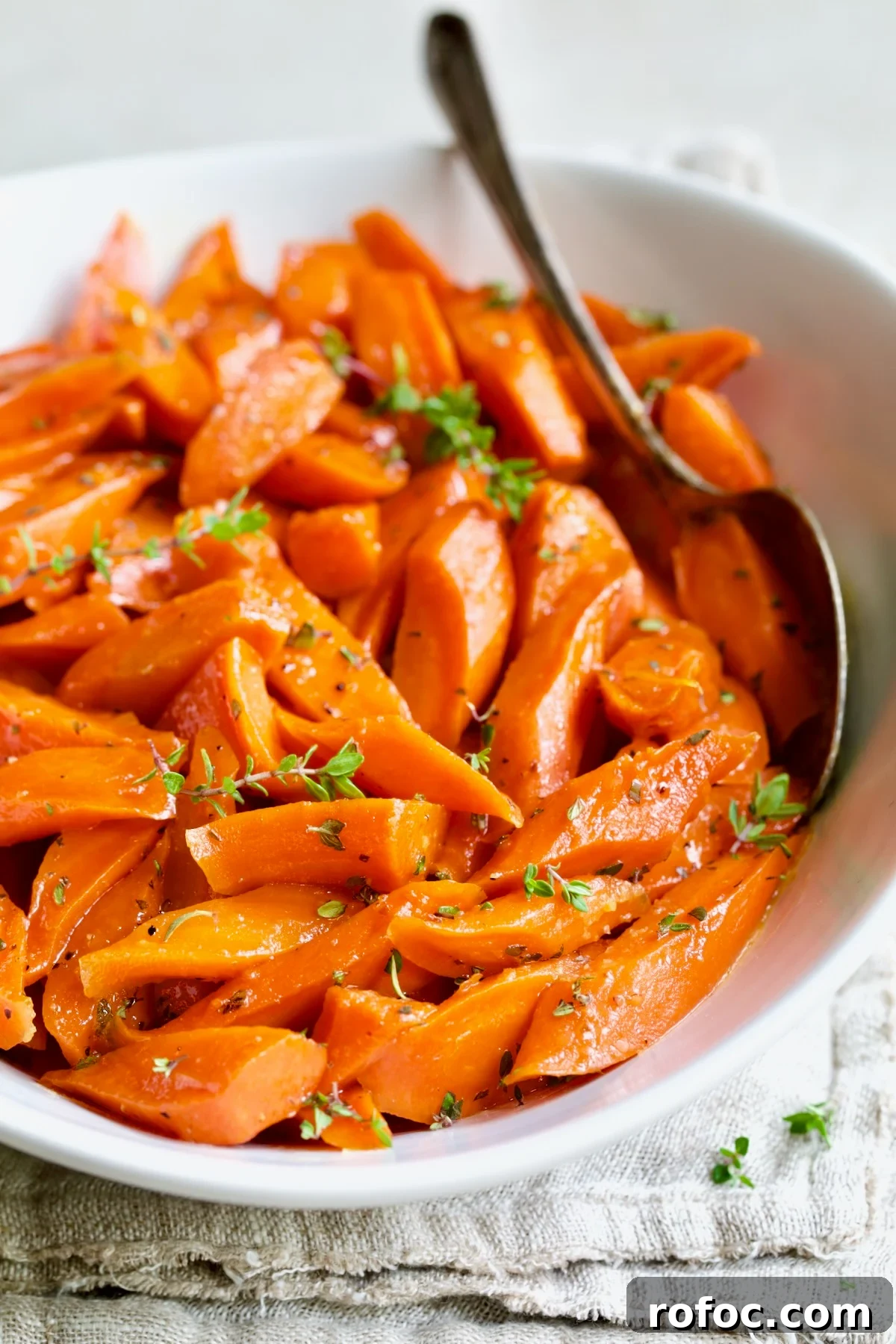 Bourbon-Glazed Carrots with Honey and Fresh Thyme 12 Bourbon-Glazed Carrots with Honey in white serving bowl with serving spoon garnished with fresh thyme.