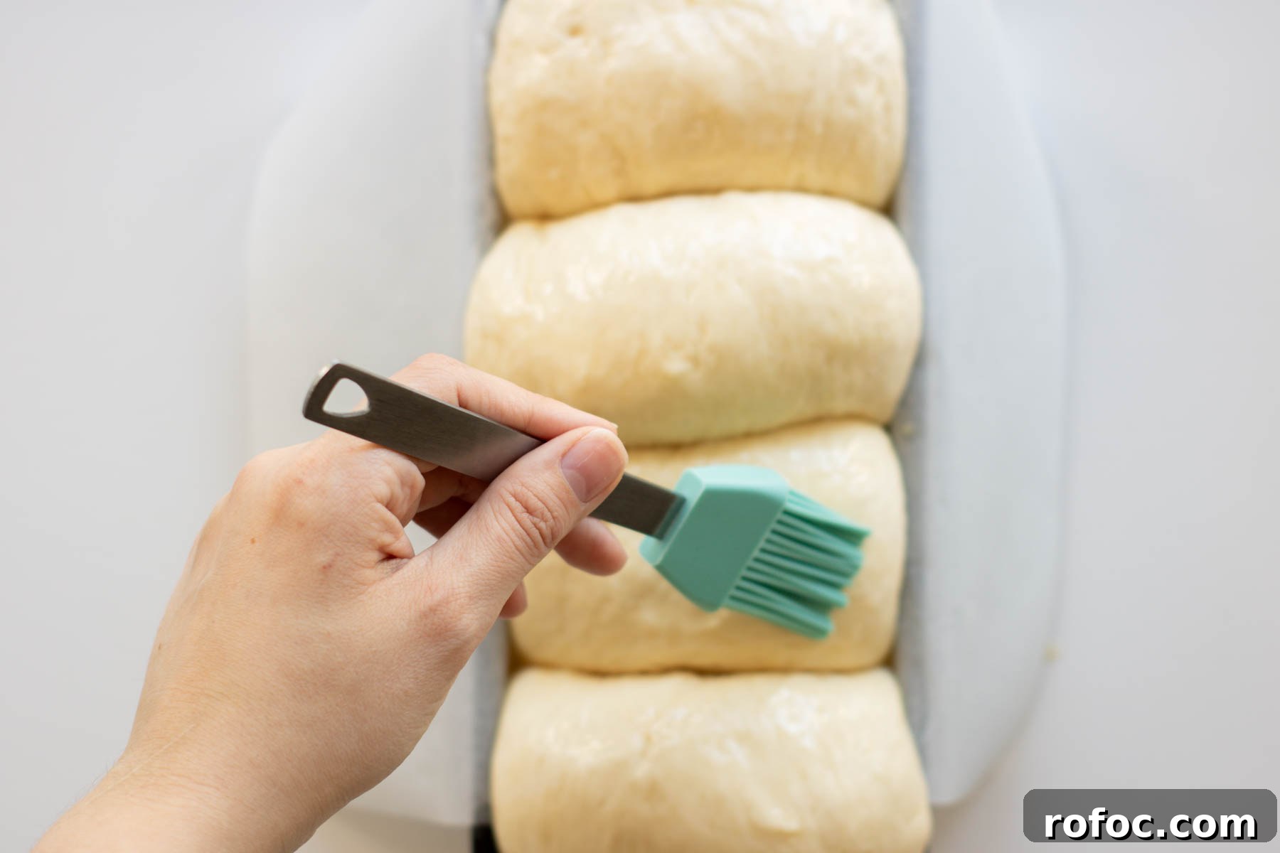 Vegan Brioche Recipe: Soft, Fluffy Egg-Free Bread 4 Hand brushing dough with maple syrup and plant-based milk wash.