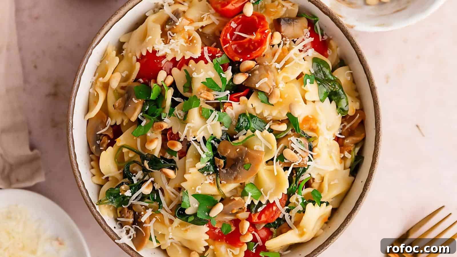 23 Vegetarian Dinners That Even Meat Eaters Will Love 16 A bowl of farfalle pasta is topped with cherry tomatoes, spinach, mushrooms, grated cheese, pine nuts, and parsley, accompanied by a fork and spoon on the side.