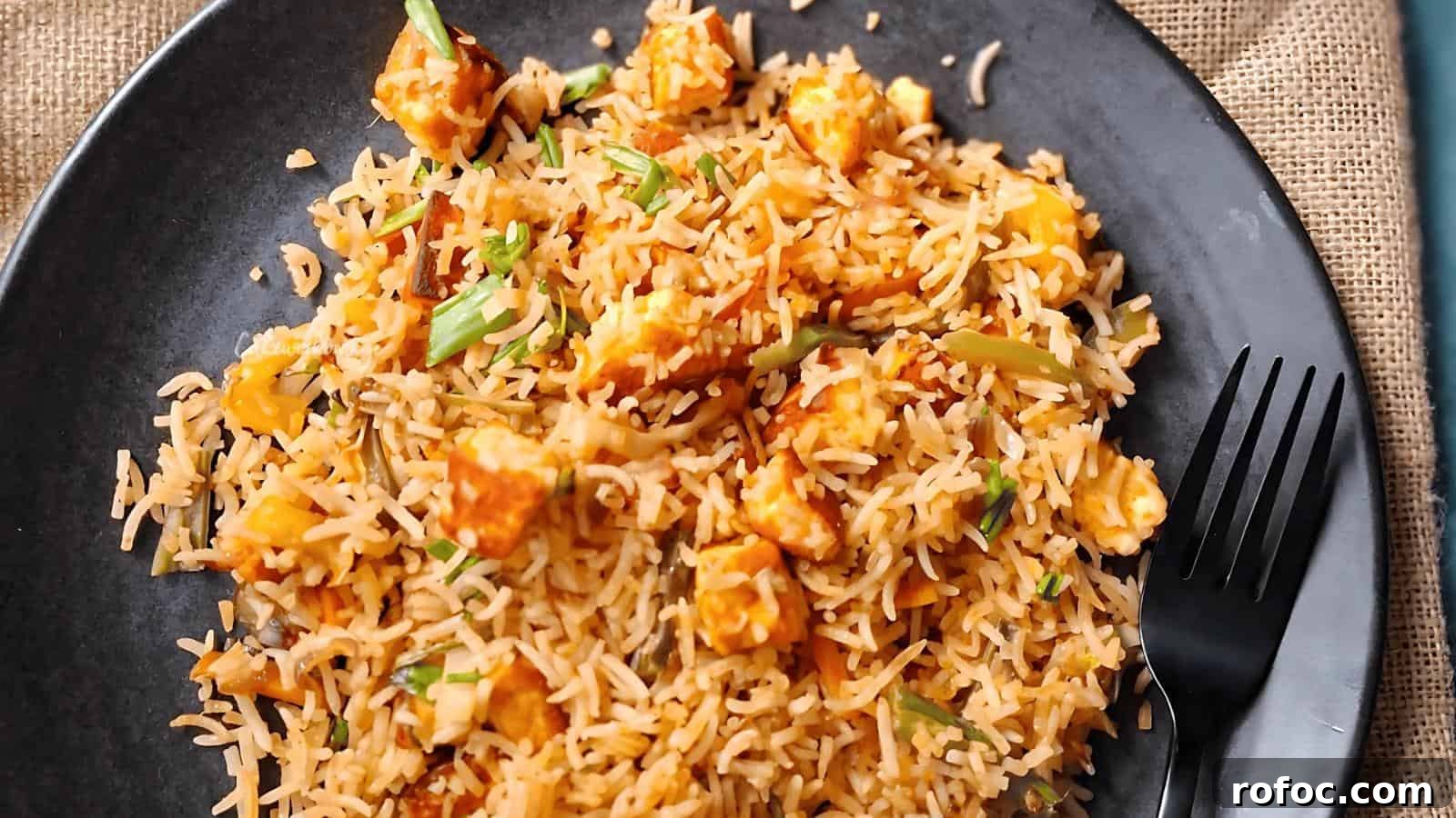 23 Vegetarian Dinners That Even Meat Eaters Will Love 18 A black plate with rice mixed with chunks of paneer, vegetables, and spices, accompanied by a fork on the side.