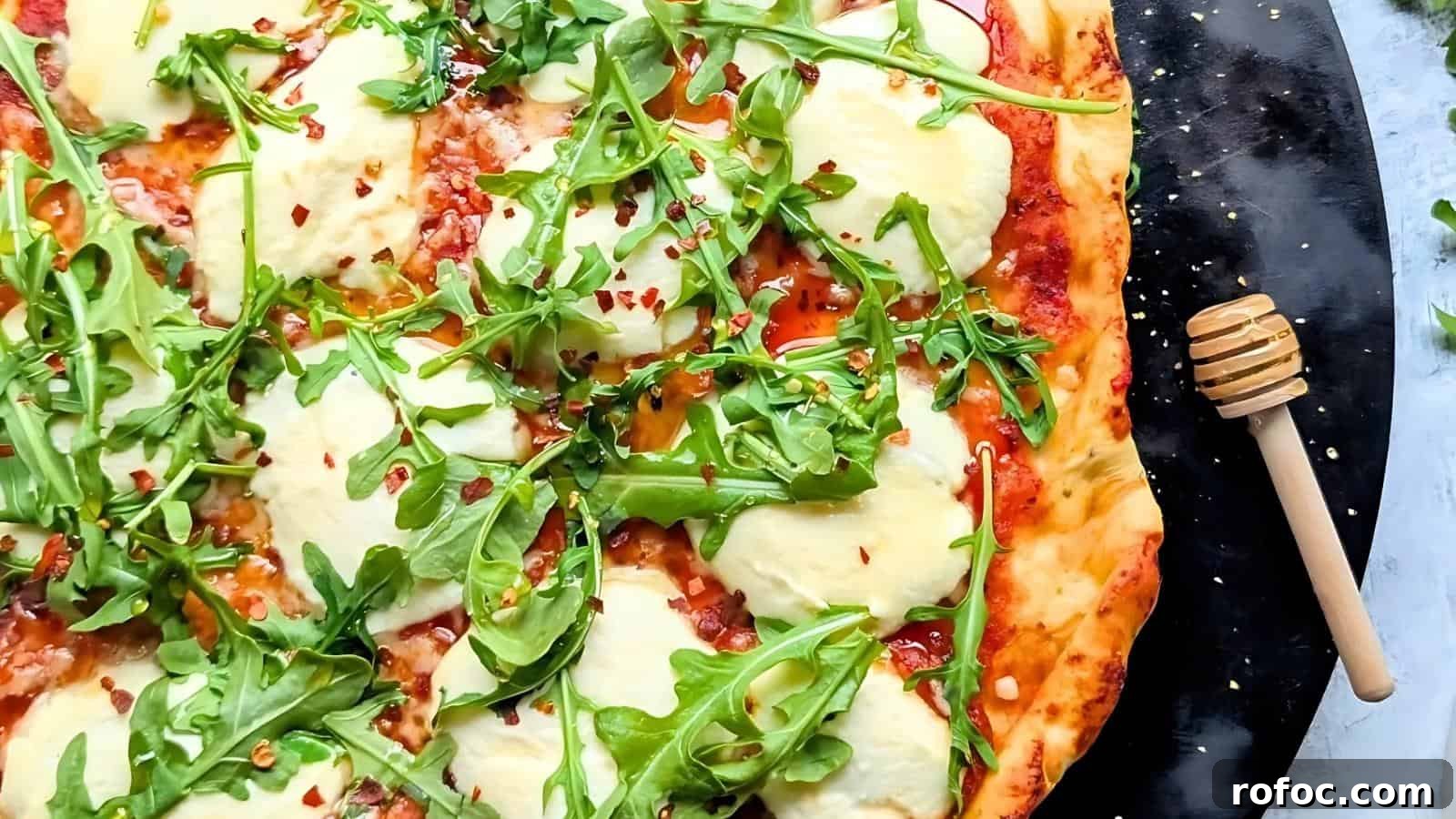 23 Vegetarian Dinners That Even Meat Eaters Will Love 19 Pizza topped with arugula, cheese, and crushed red pepper flakes, arranged on a black surface with a honey dipper nearby.