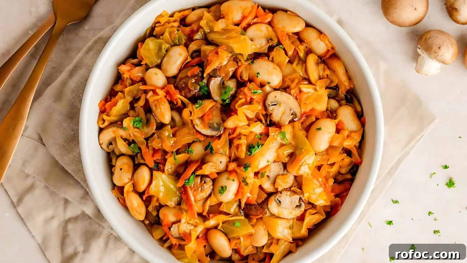 23 Vegetarian Dinners That Even Meat Eaters Will Love 24 A bowl of mixed vegetables including mushrooms, cabbage, and carrots, garnished with parsley, is placed on a beige cloth beside gold-colored cutlery.