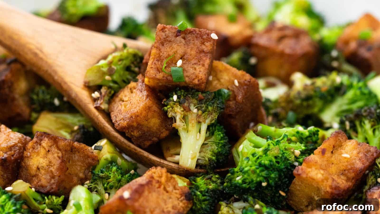 23 Vegetarian Dinners That Even Meat Eaters Will Love 5 Close-up of roasted broccoli and tofu cubes tossed with sesame seeds in a wooden spoon, set against a blurred background.