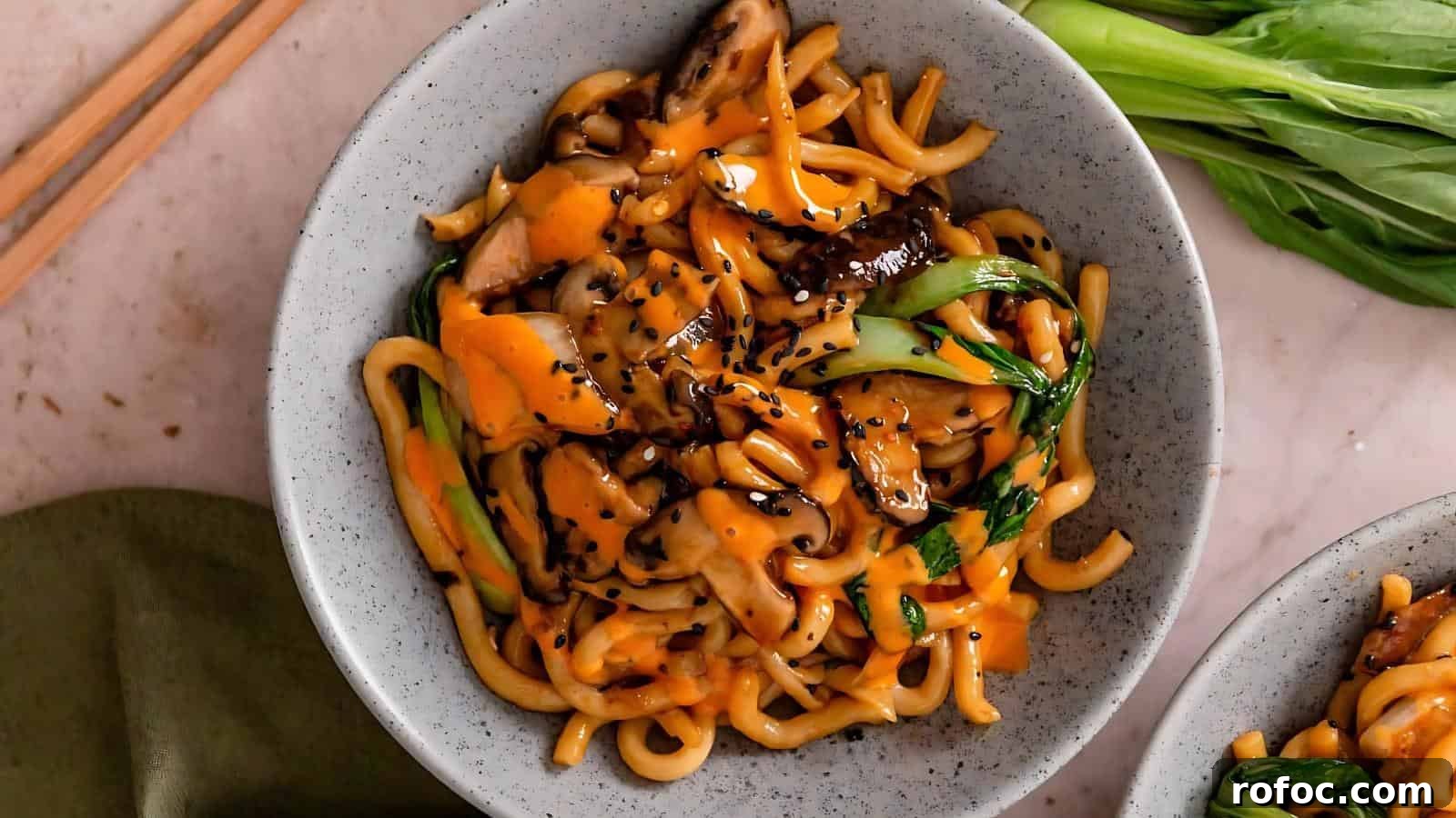 23 Vegetarian Dinners That Even Meat Eaters Will Love 6 A bowl of udon noodles with vegetables and mushrooms, topped with orange sauce and black sesame seeds. Chopsticks and bok choy are next to the bowl.