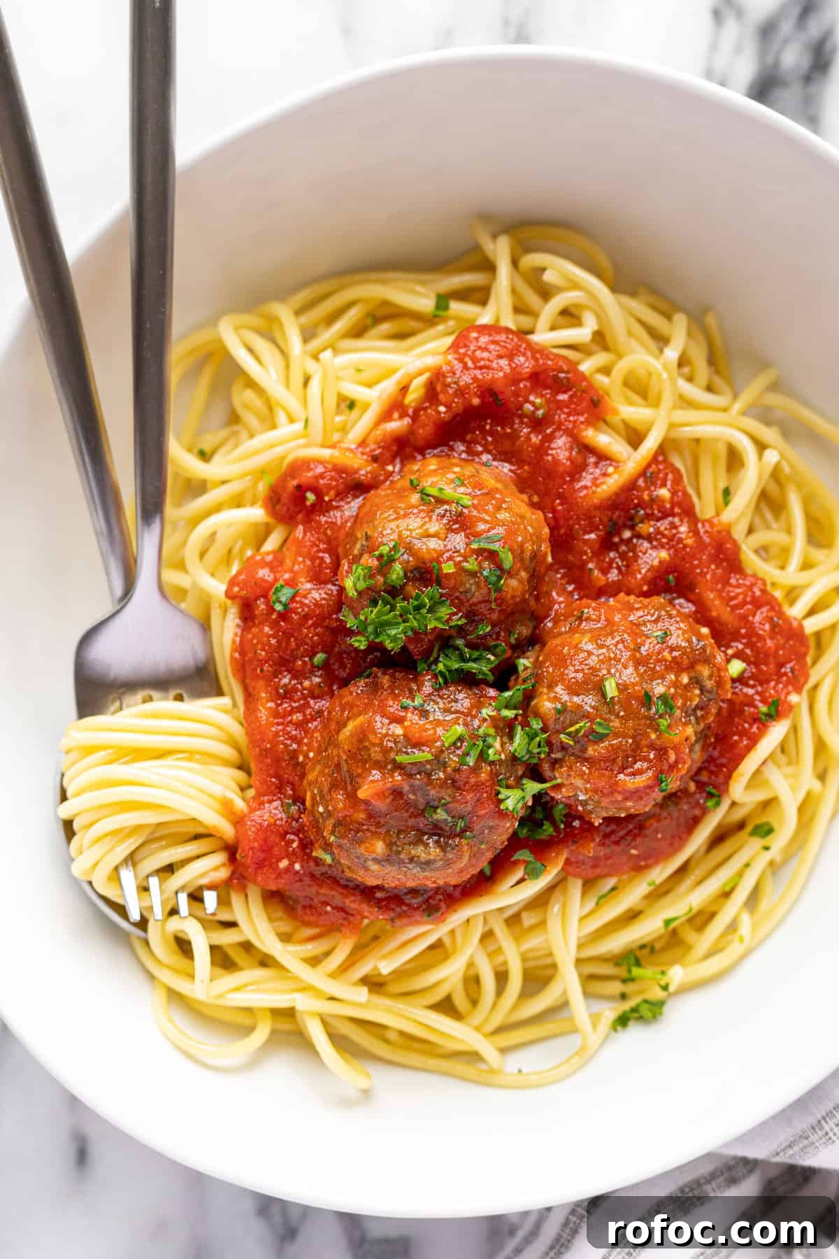 Authentic Italian Meatballs Recipe Ready in 30 Minutes 13 White bowl filled with spaghetti and homemade meatballs with marinara sauce and parsley.