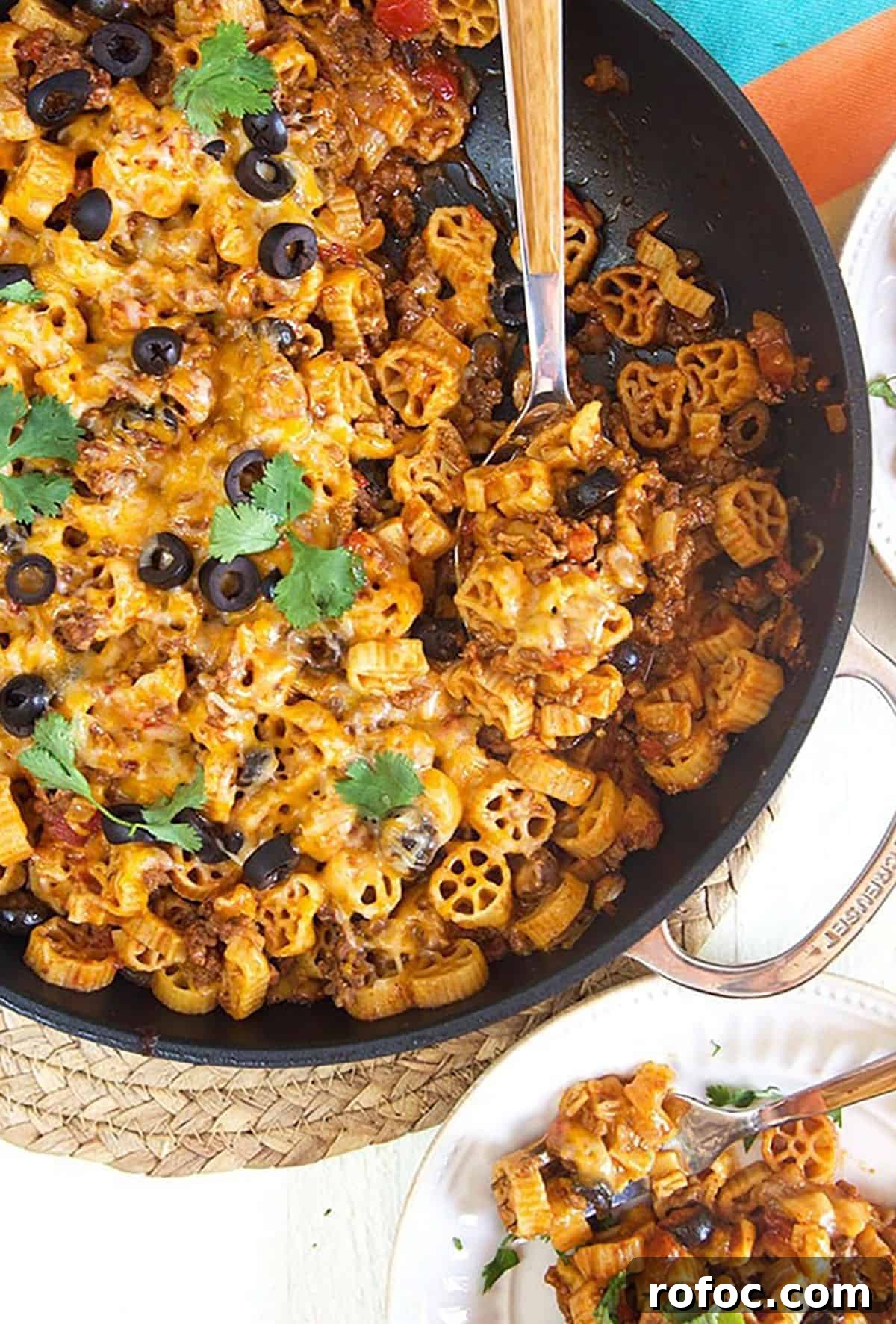 Cheesy Taco Pasta Recipe: One-Pot Mexican-Inspired Dinner 2 Overhead shot of taco pasta in a black skillet with a wooden spoon on a white background.