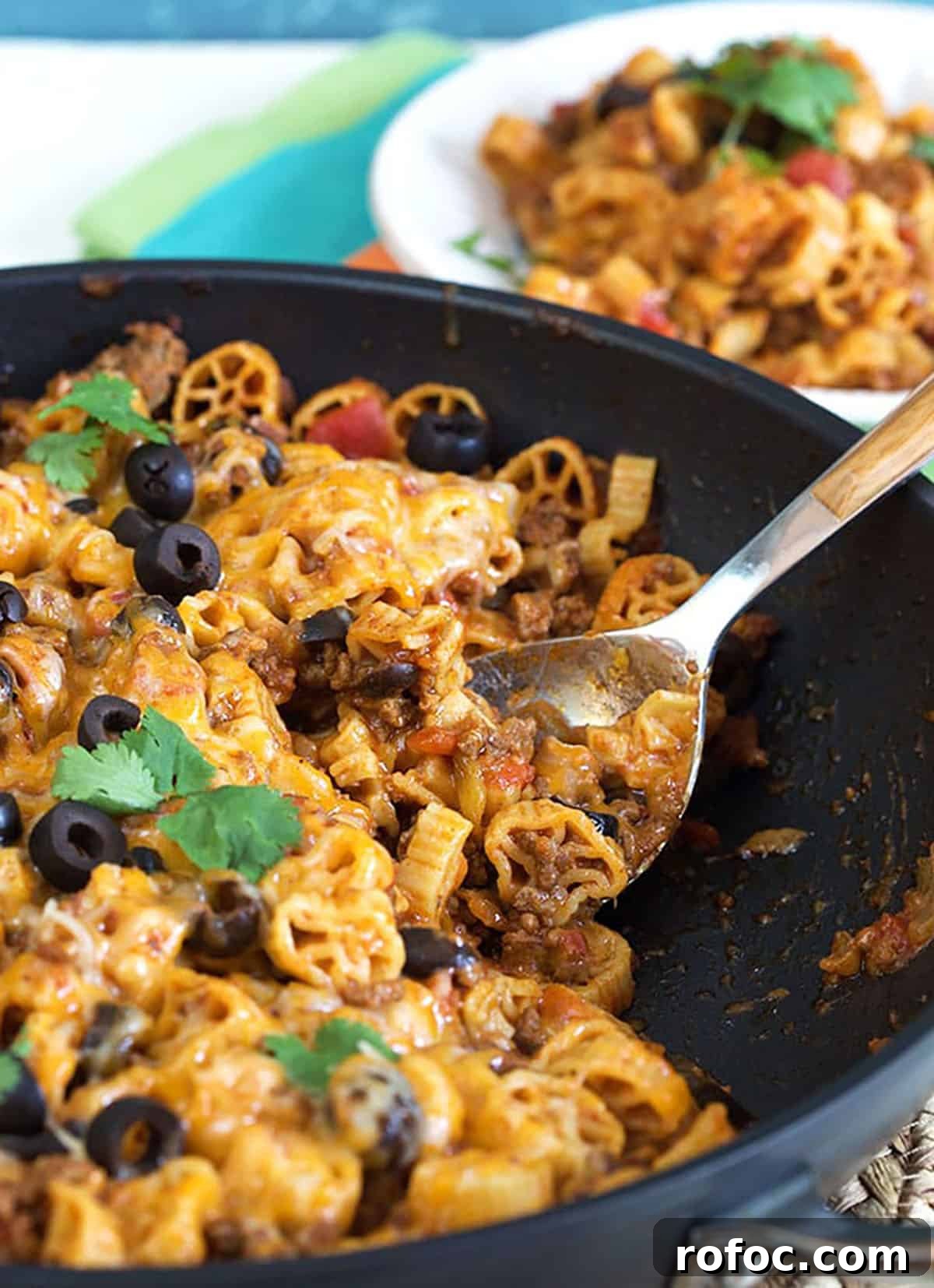 Cheesy Taco Pasta Recipe: One-Pot Mexican-Inspired Dinner 3 close up of taco pasta in a black skillet with a wooden spoon.