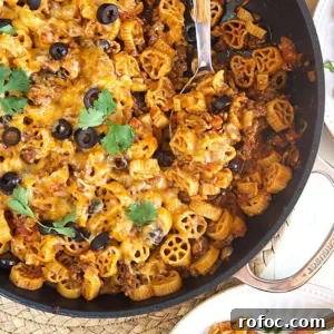 Cheesy Taco Pasta Recipe: One-Pot Mexican-Inspired Dinner 7 Overhead shot of taco pasta in a black skillet with a wooden spoon on a white background.