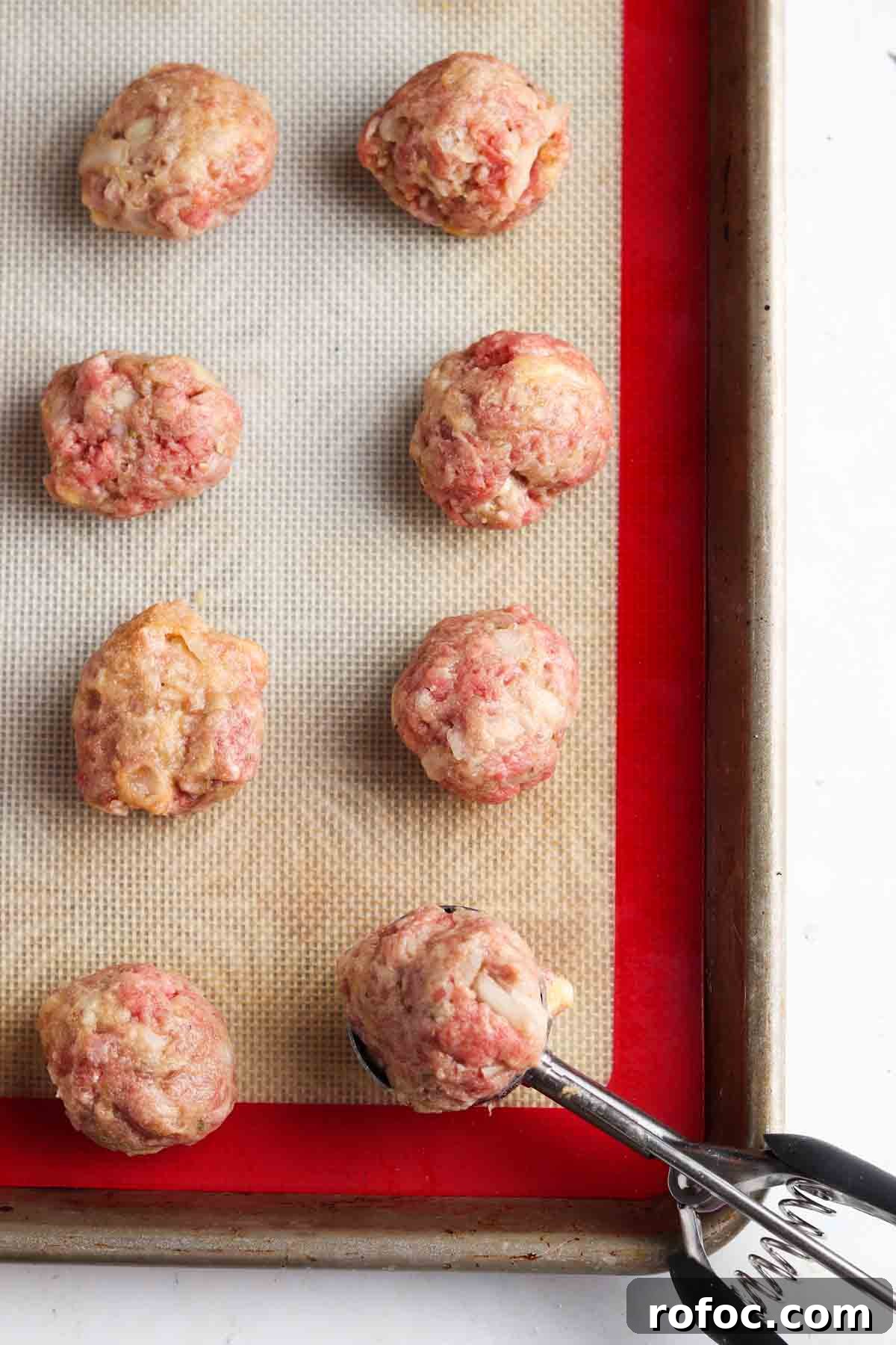Gluten-Free Meatballs: Savory, Tender Recipe for Dinner 8 Raw ground beef meatballs on a baking tray with a cookie scooper.