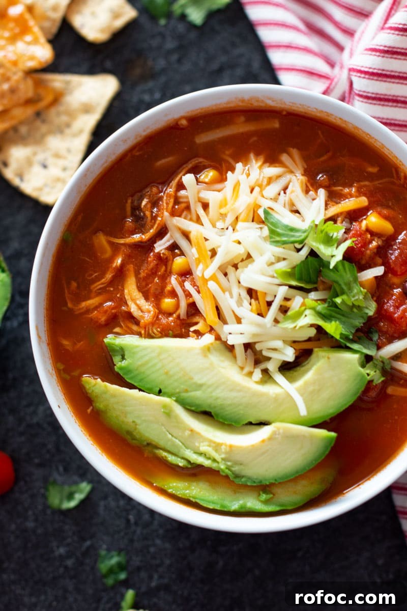 Close up of a bowl of chicken tortilla soup topped with cheese, avocado, and cilantro.