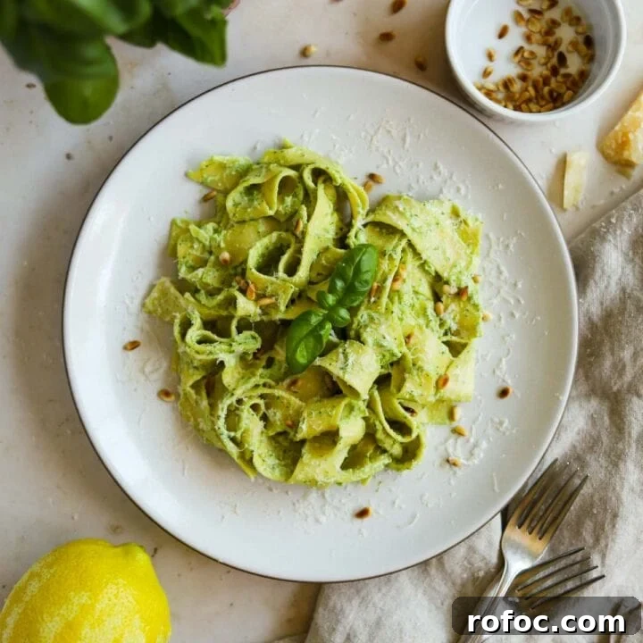 Creamy pesto pasta on a plate with toasted pine nuts and basil.