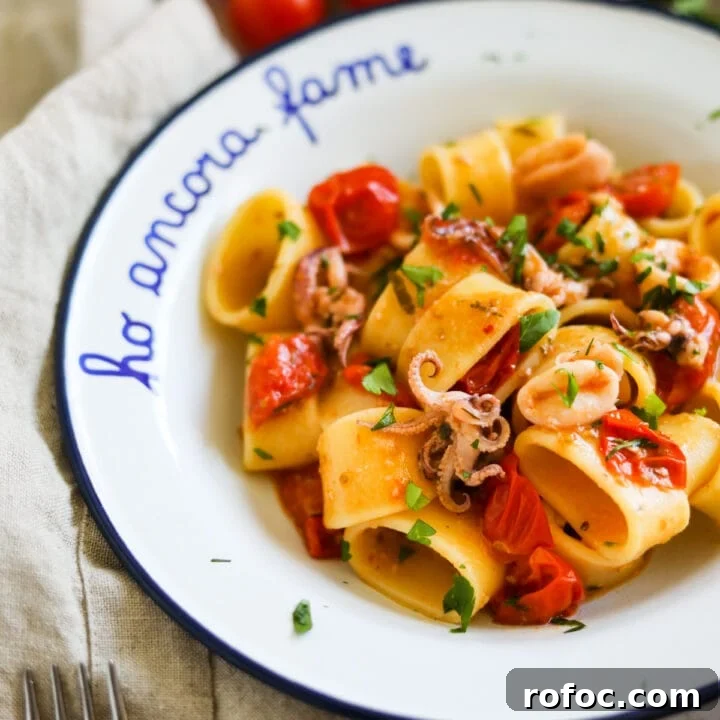 Closeup shot of Calamarata calamari and tomato pasta in a white bowl.