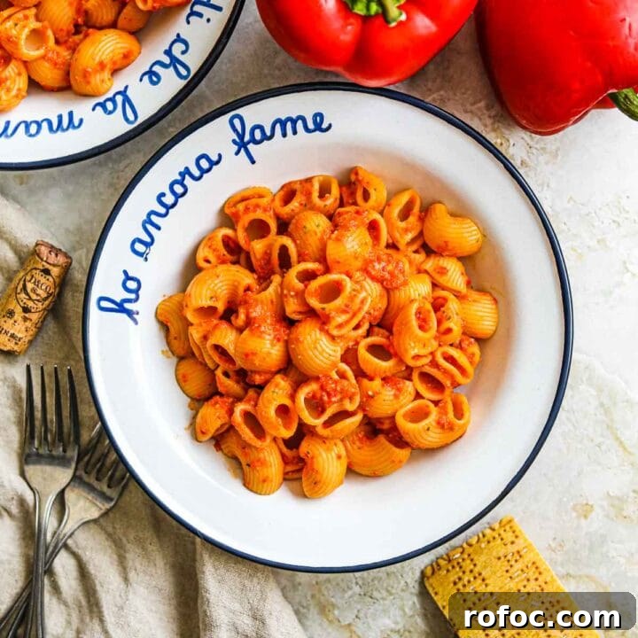 Roasted red pepper pesto pasta in a bowl with roasted red bell pepper and parmigiano-reggiano.