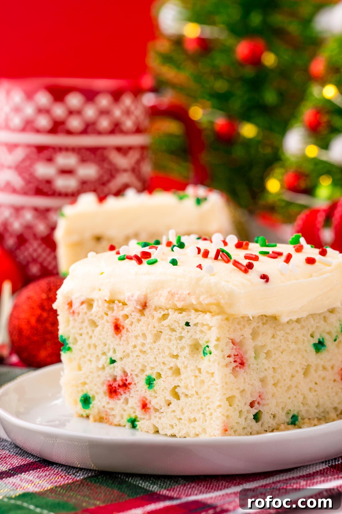 Classic Christmas Cake Recipe: Moist Fruit Cake for the Holidays 2 Close up photo of a slice of christmas cake on a white plate with holiday decor in the background.