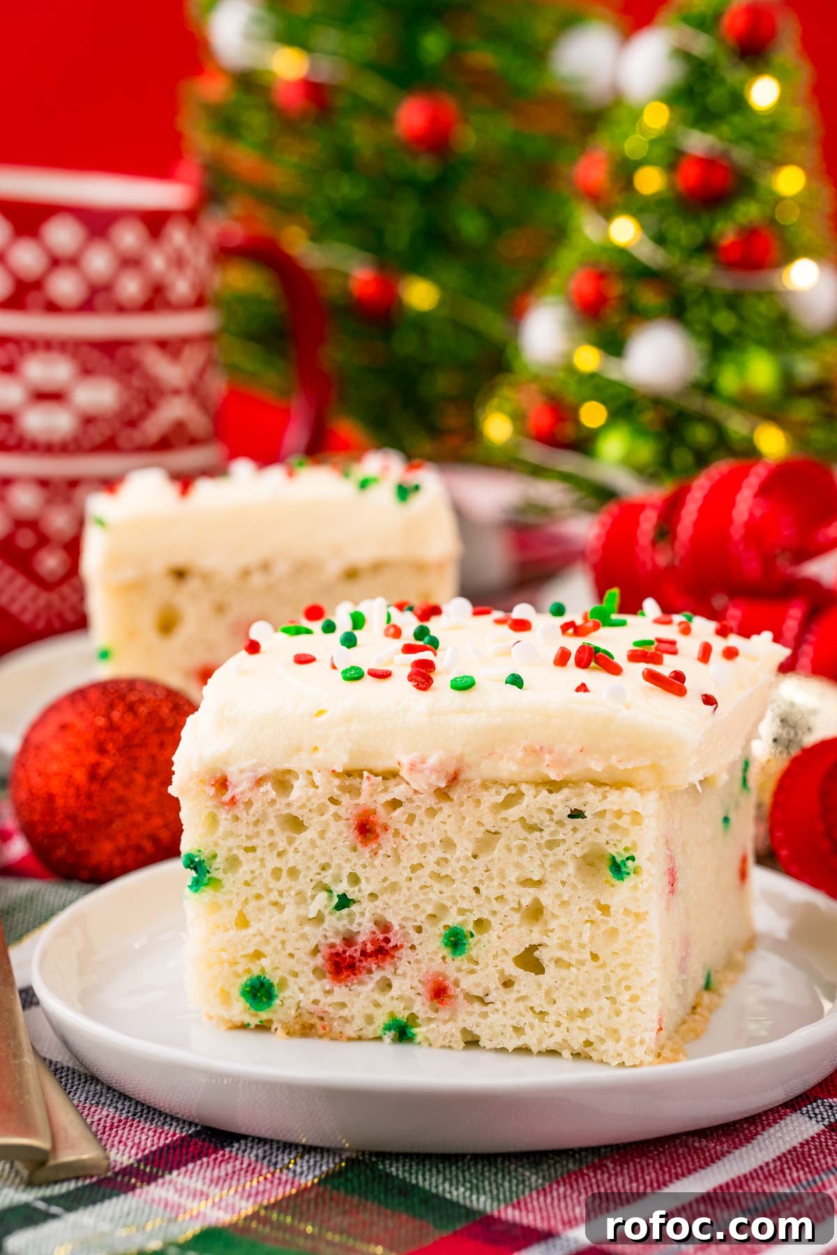 Classic Christmas Cake Recipe: Moist Fruit Cake for the Holidays 6 A slice of funfetti Christmas cake on a white plate on a holiday napkin with decor in the background.