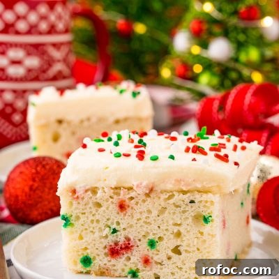 Classic Christmas Cake Recipe: Moist Fruit Cake for the Holidays 7 A slice of funfetti Christmas cake on a white plate on a holiday napkin with decor in the background.