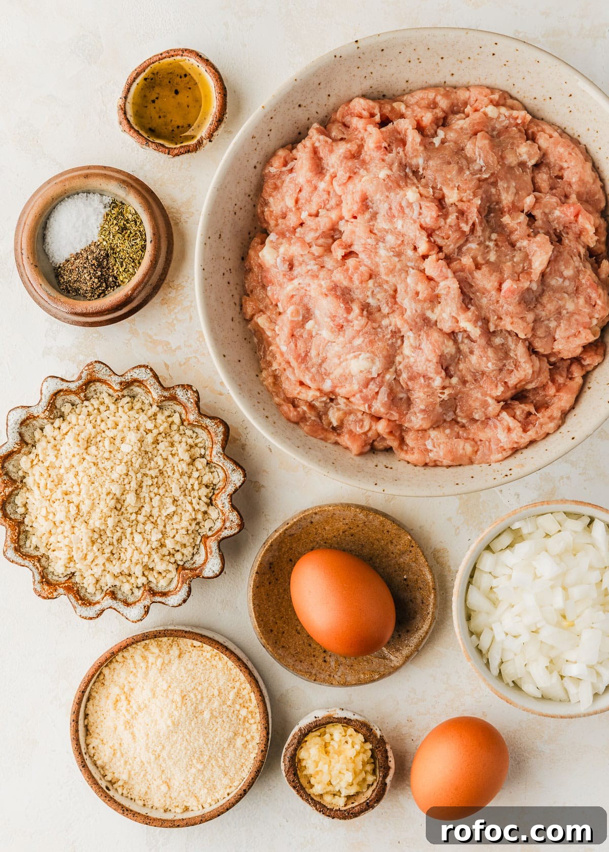 Crispy Air Fryer Chicken Meatballs Recipe 3 White and brown bowls of ground meat, spices, breadcrumbs, parmesan, onion, eggs, garlic, and oil on a tan counter
