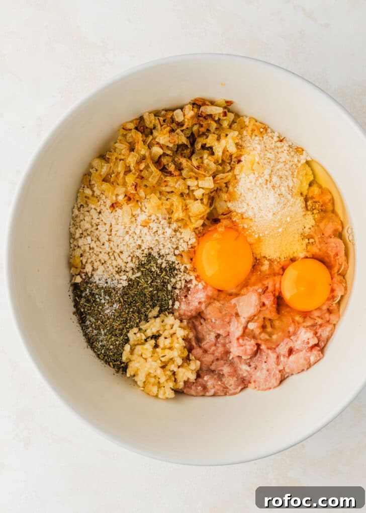 Crispy Air Fryer Chicken Meatballs Recipe 5 A white bowl of ground meat, breadcrumbs, parmesan, herbs, onions, and eggs on a white counter.
