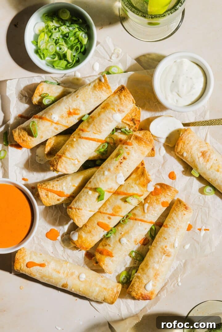 Spicy Buffalo Chicken Taquitos Recipe for Game Day Snacks 11 Buffalo chicken taquitos garnished with buffalo sauce and ranch on a large piece of parchment paper