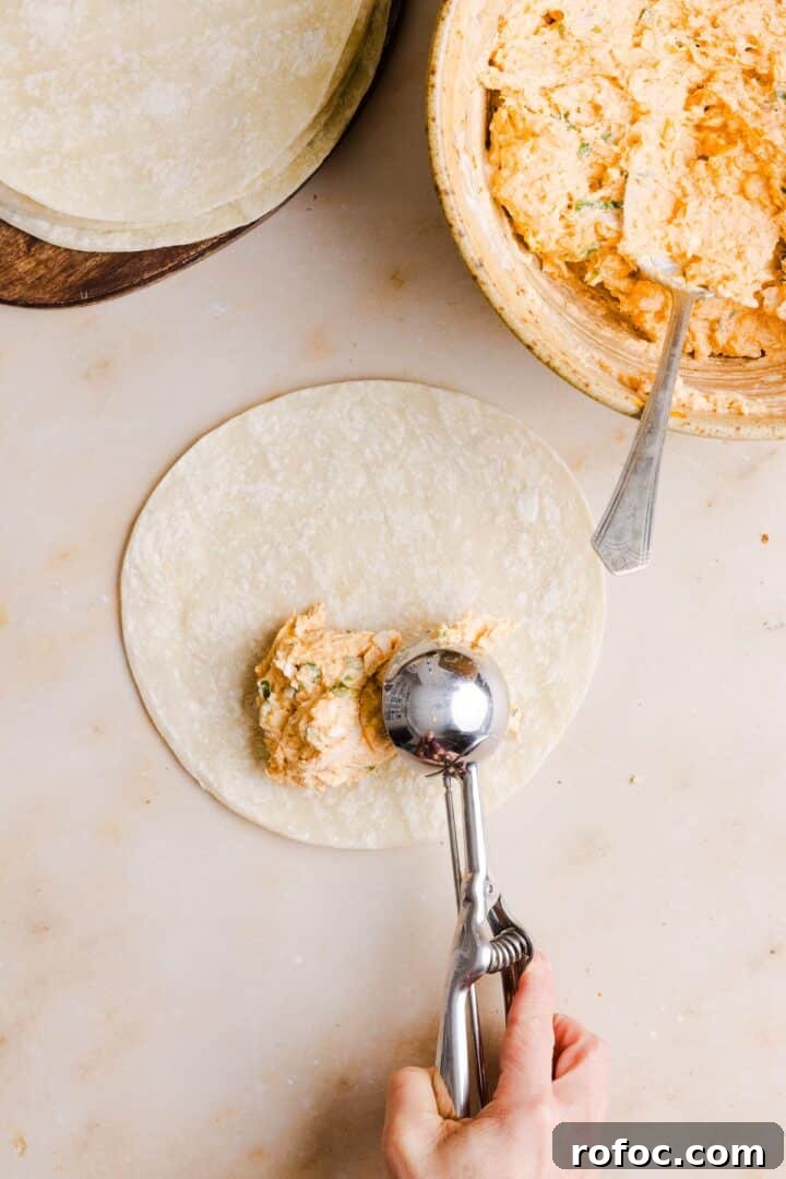 Spicy Buffalo Chicken Taquitos Recipe for Game Day Snacks 7 Cookie scoop being used to fill buffalo chicken taquito, before rolling