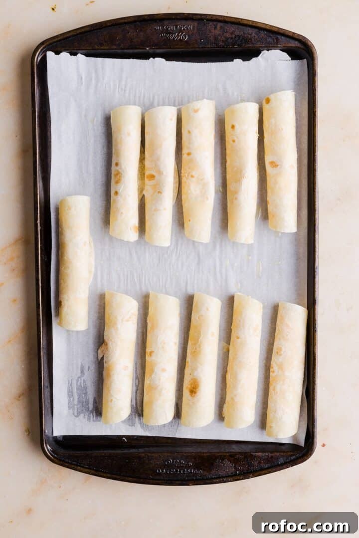 Spicy Buffalo Chicken Taquitos Recipe for Game Day Snacks 9 Buffalo chicken taquitos lined up on a baking tray before being cooked