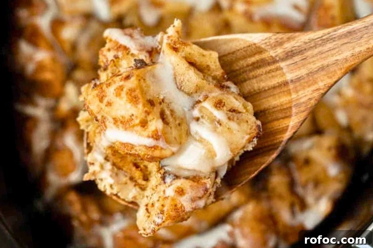 12 Delicious Easter Crockpot Recipes for a Stress-Free Holiday 2 A wooden spoon serving a slice of cinnamon roll casserole, showcasing its fluffy texture and creamy icing.