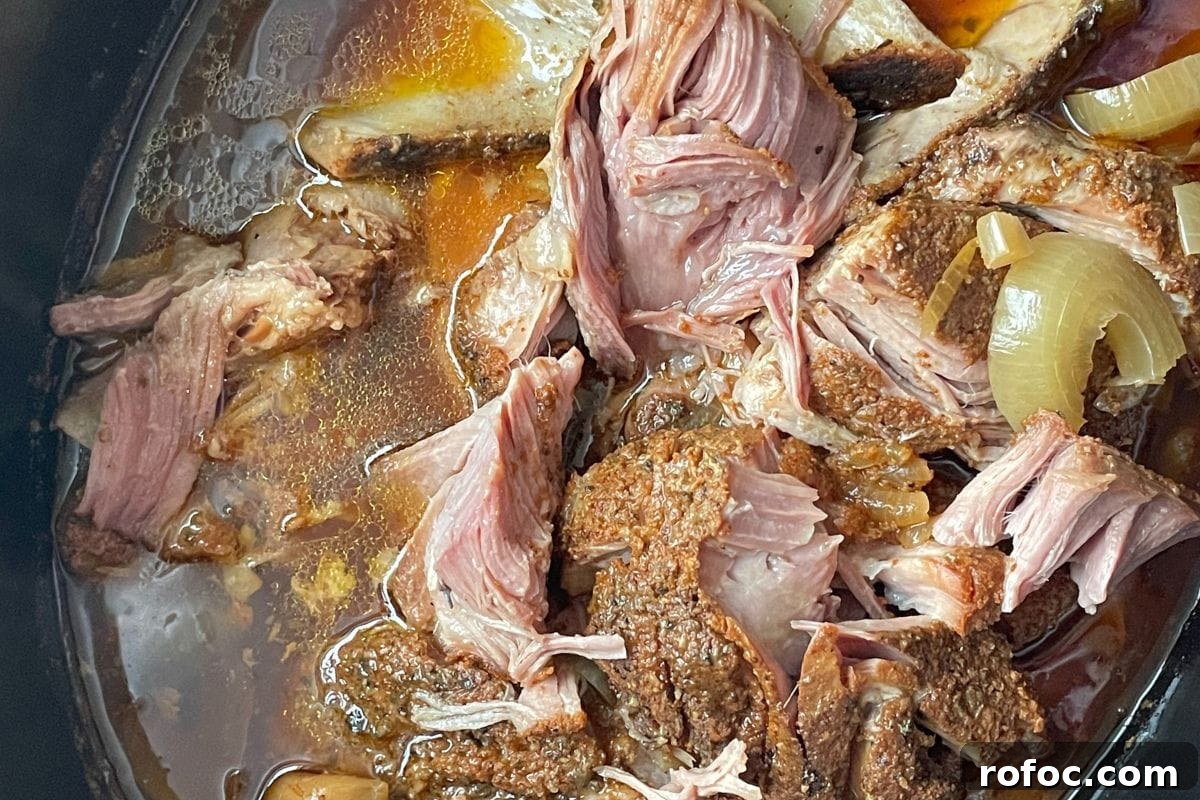 12 Delicious Easter Crockpot Recipes for a Stress-Free Holiday 11 Close-up of tender slow-cooked pork with onions in broth, showcasing the succulent textures and rich colors.